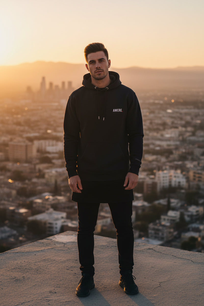 Man wearing oversized black AWARE hoodie by Mental State Wear overlooking city at sunset