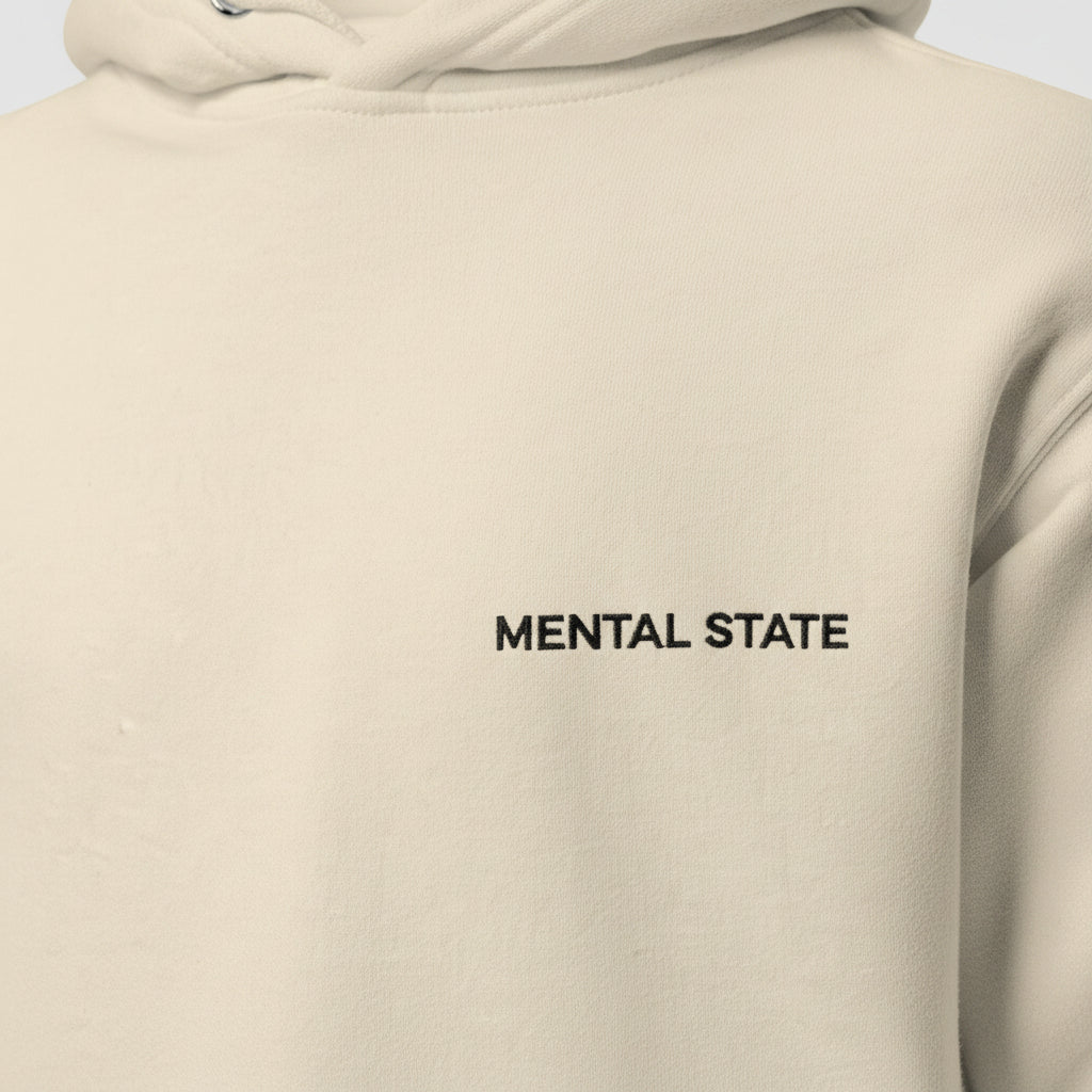 Close-up detail of embroidered Mental State logo on oversized beige hoodie, premium stitching quality, minimalist luxury streetwear aesthetic.